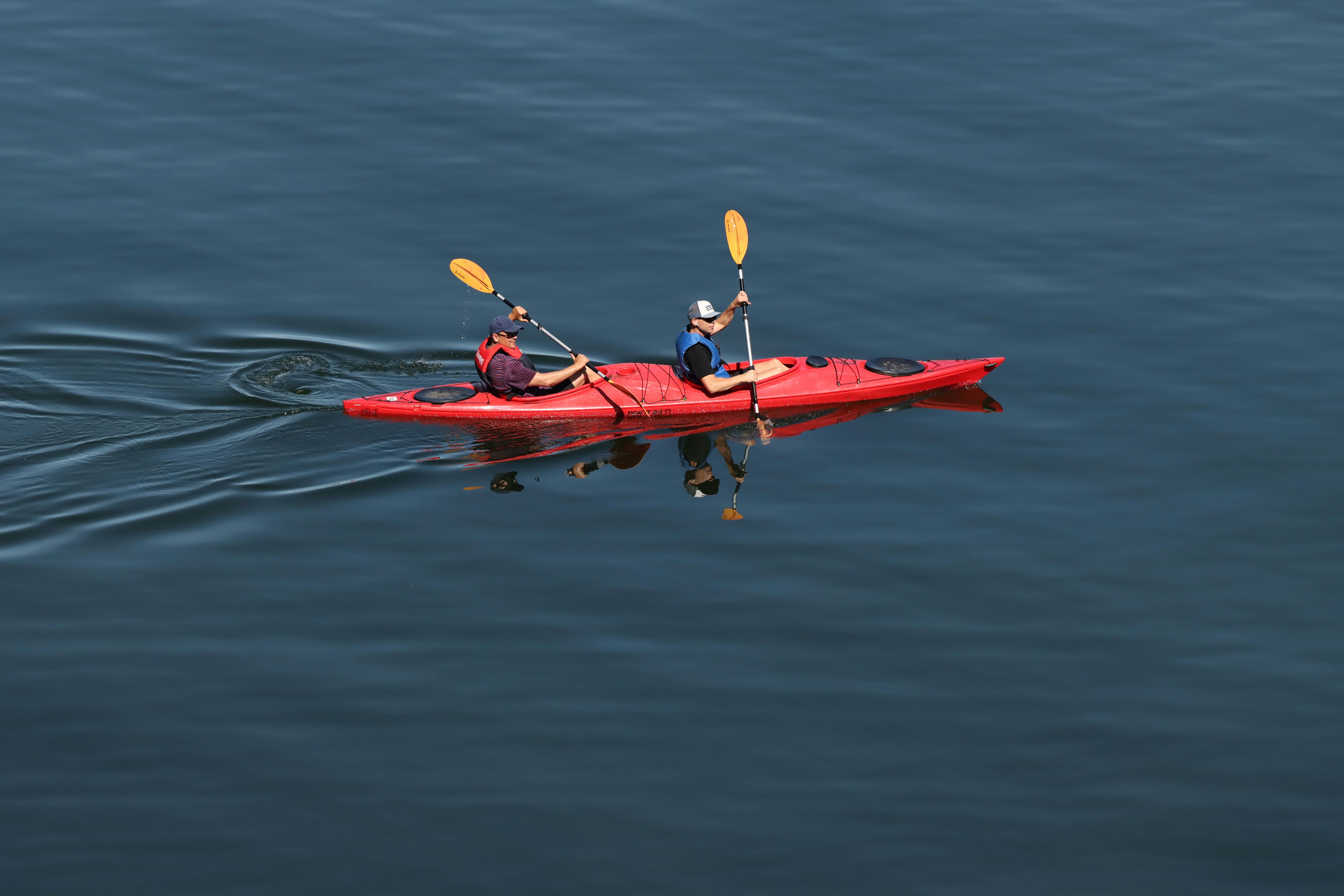 Two people kayaking in a red kayak on a serene lake in Sweden. Outdoor recreation and adventure.