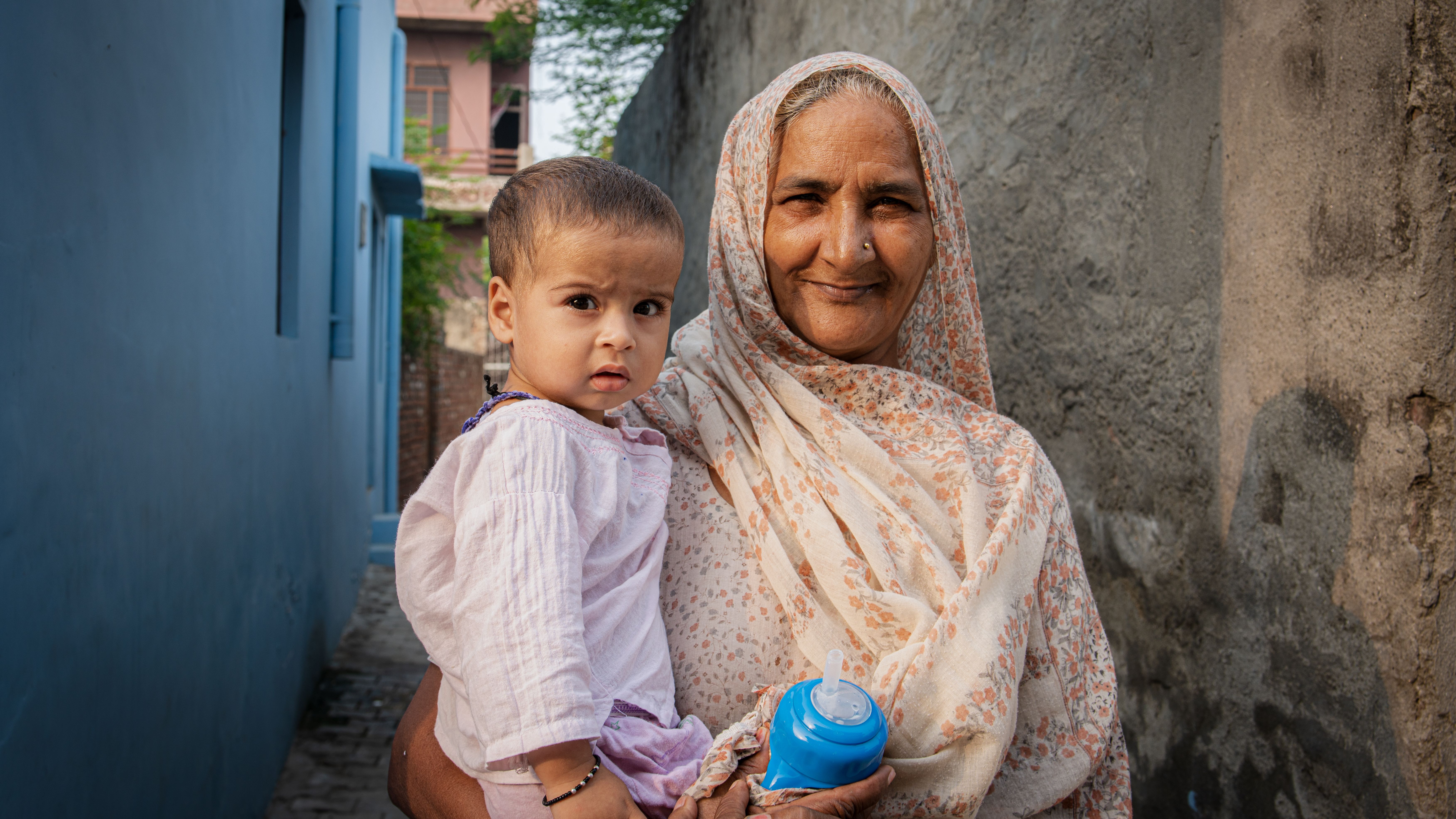 An elderly woman holding a baby in a peaceful village setting in Rohtak, India.