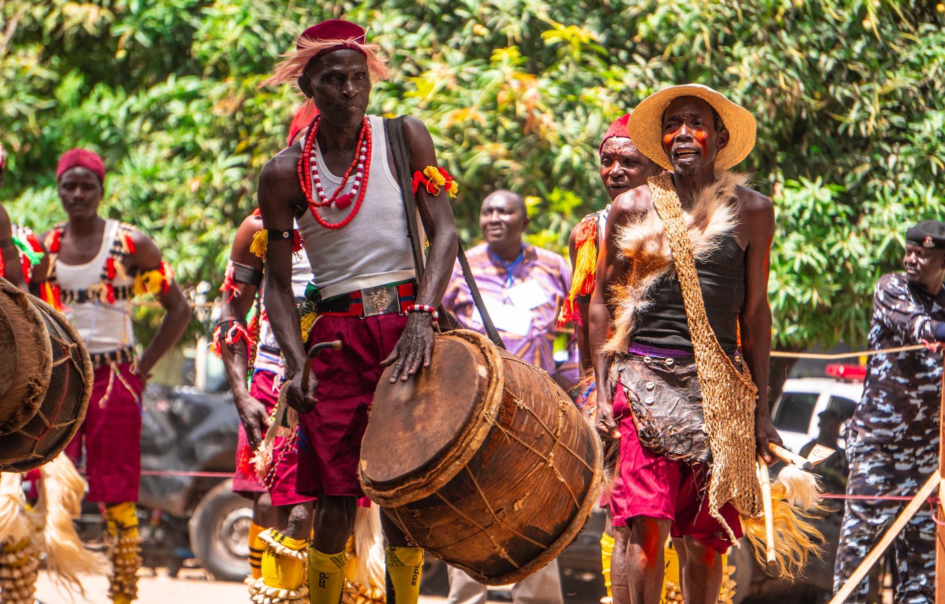 Group of African men in traditional attire performing with drums during a vibrant outdoor cultural festival.