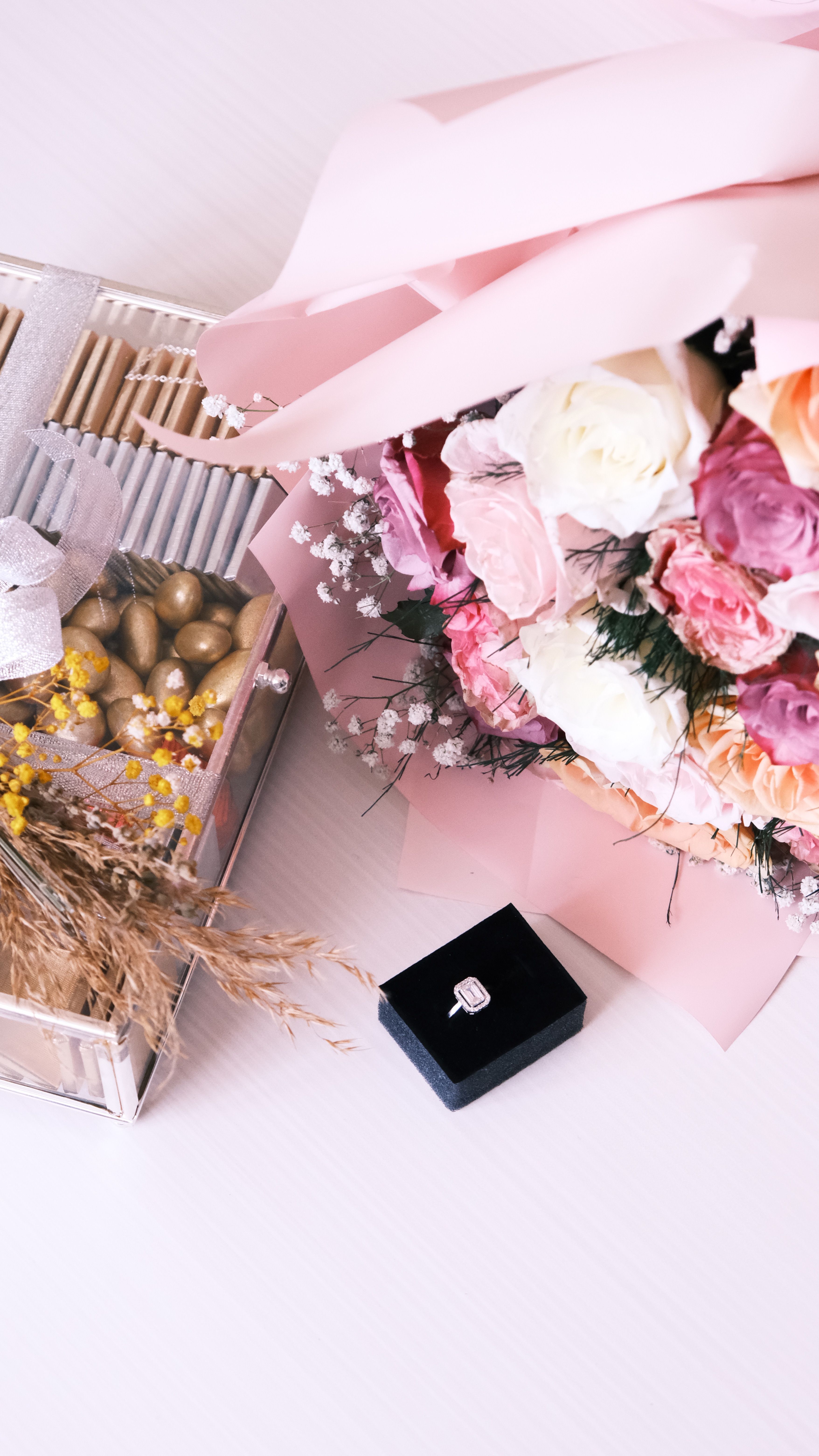 A romantic setting with a colorful bouquet, engagement ring, and luxury chocolates.