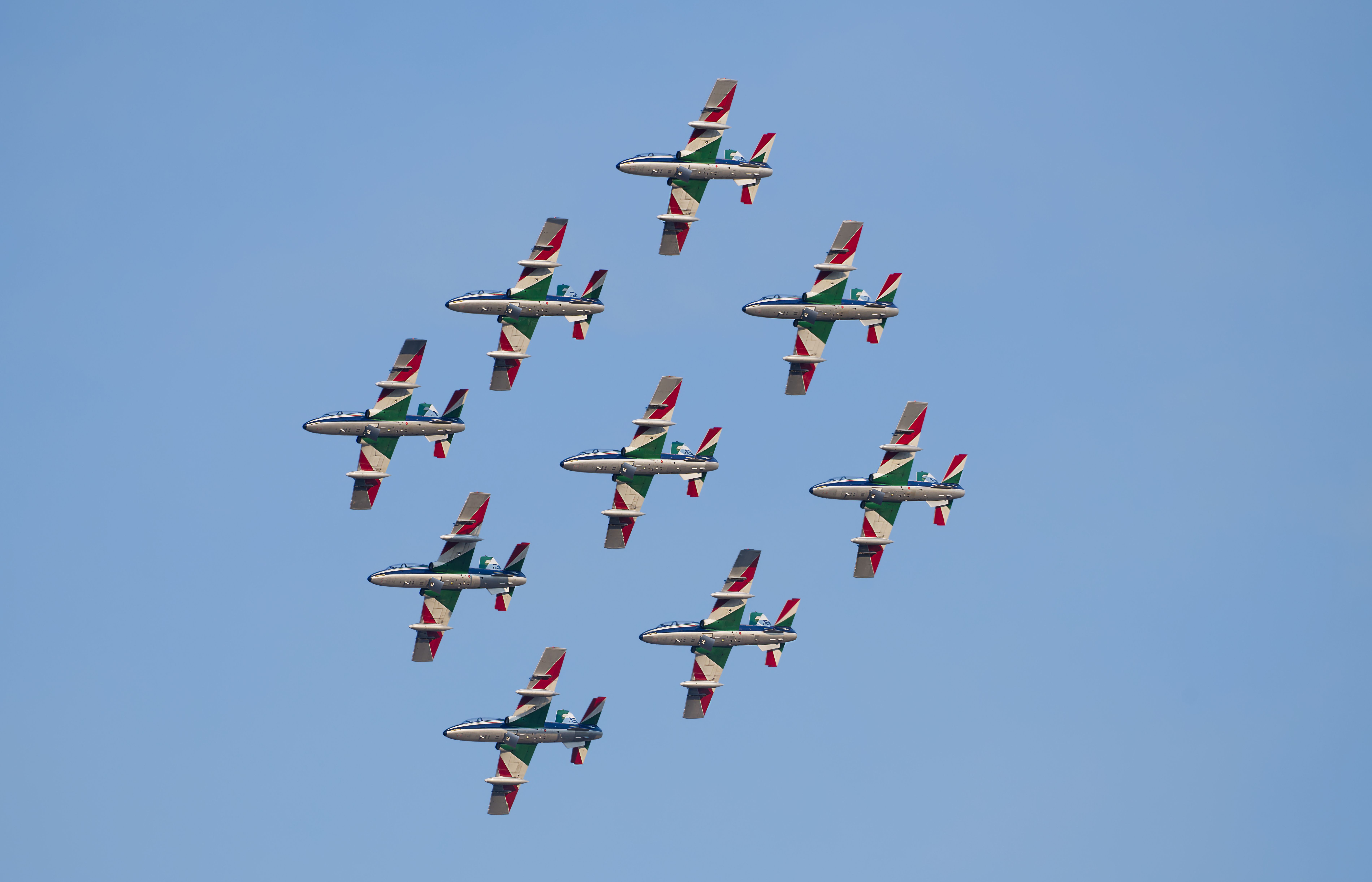 Aerial view of a military jet team performing a precise aerobatic formation under clear skies.