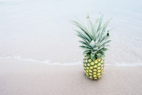 Free A tropical pineapple sits on the sandy shoreline, blending nature with beach vibes. Stock Photo