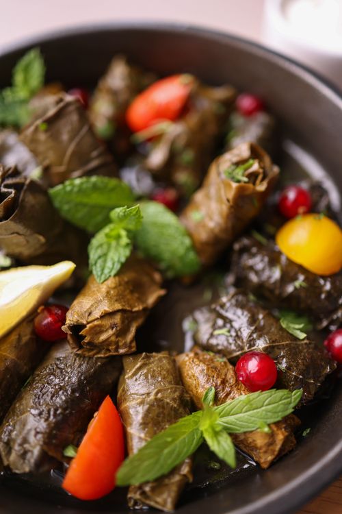 Free Delicious Mediterranean stuffed grape leaves garnished with fresh herbs and colorful vegetables. Stock Photo