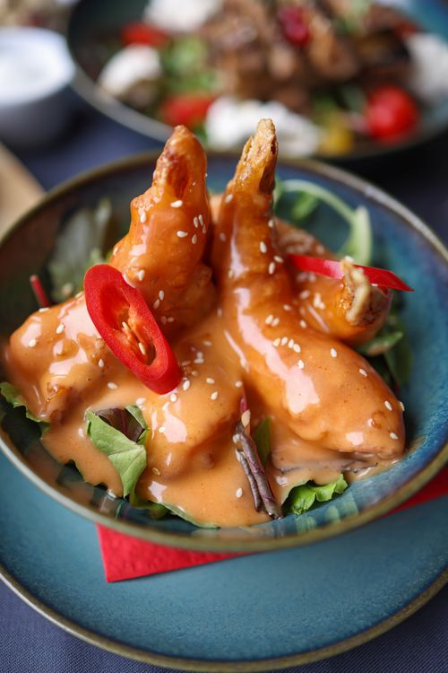 Free Close-up of spicy chicken wings drizzled with chili sauce in a bowl, garnished with greens and red peppers. Stock Photo