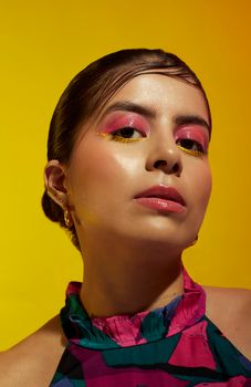 Stunning portrait of a woman with vibrant makeup and colorful attire on a yellow background.