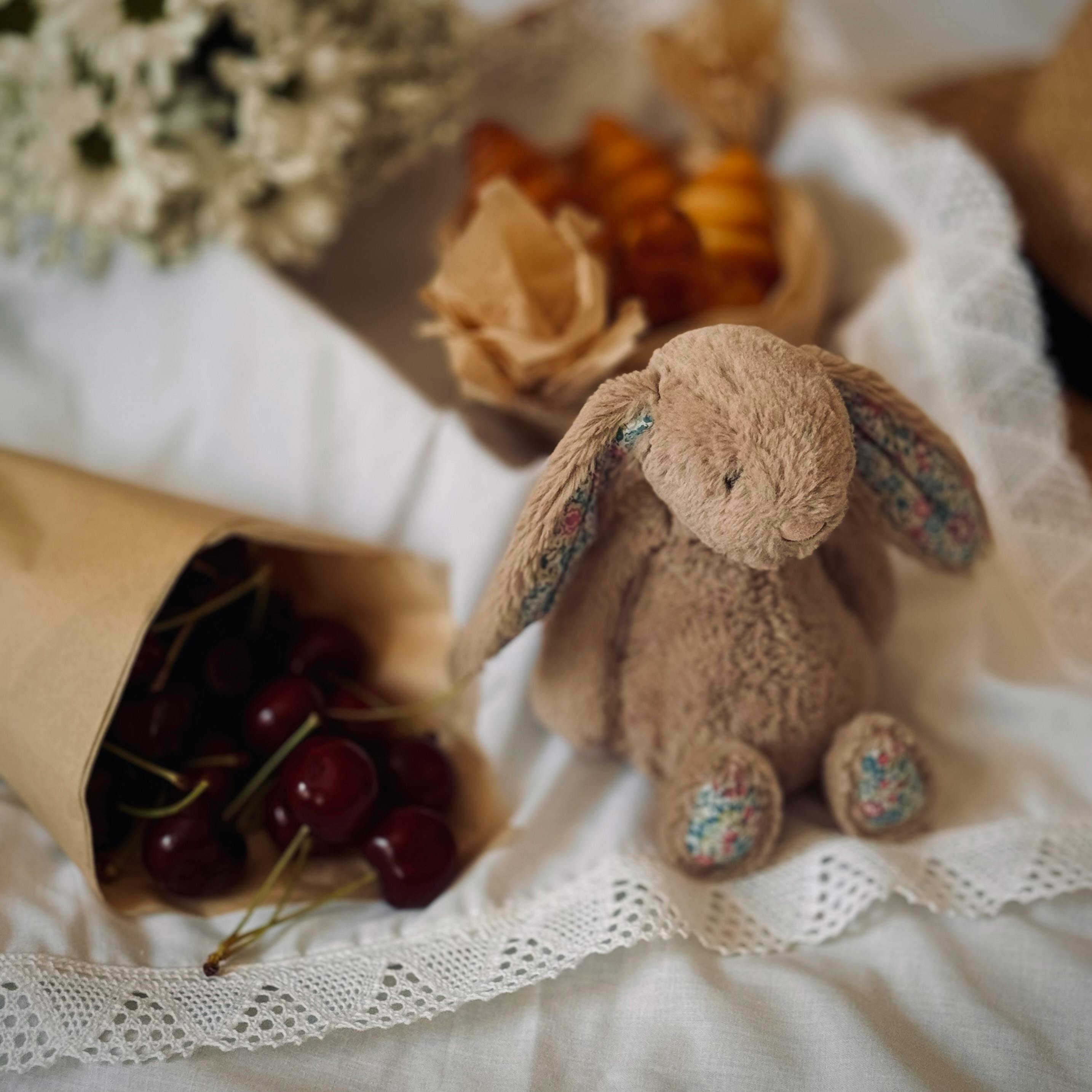 a stuffed rabbit sitting on a bed with cherries