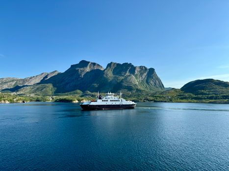 A ferry travels across a clear fjord against a backdrop of stunning mountains under a summer sky.