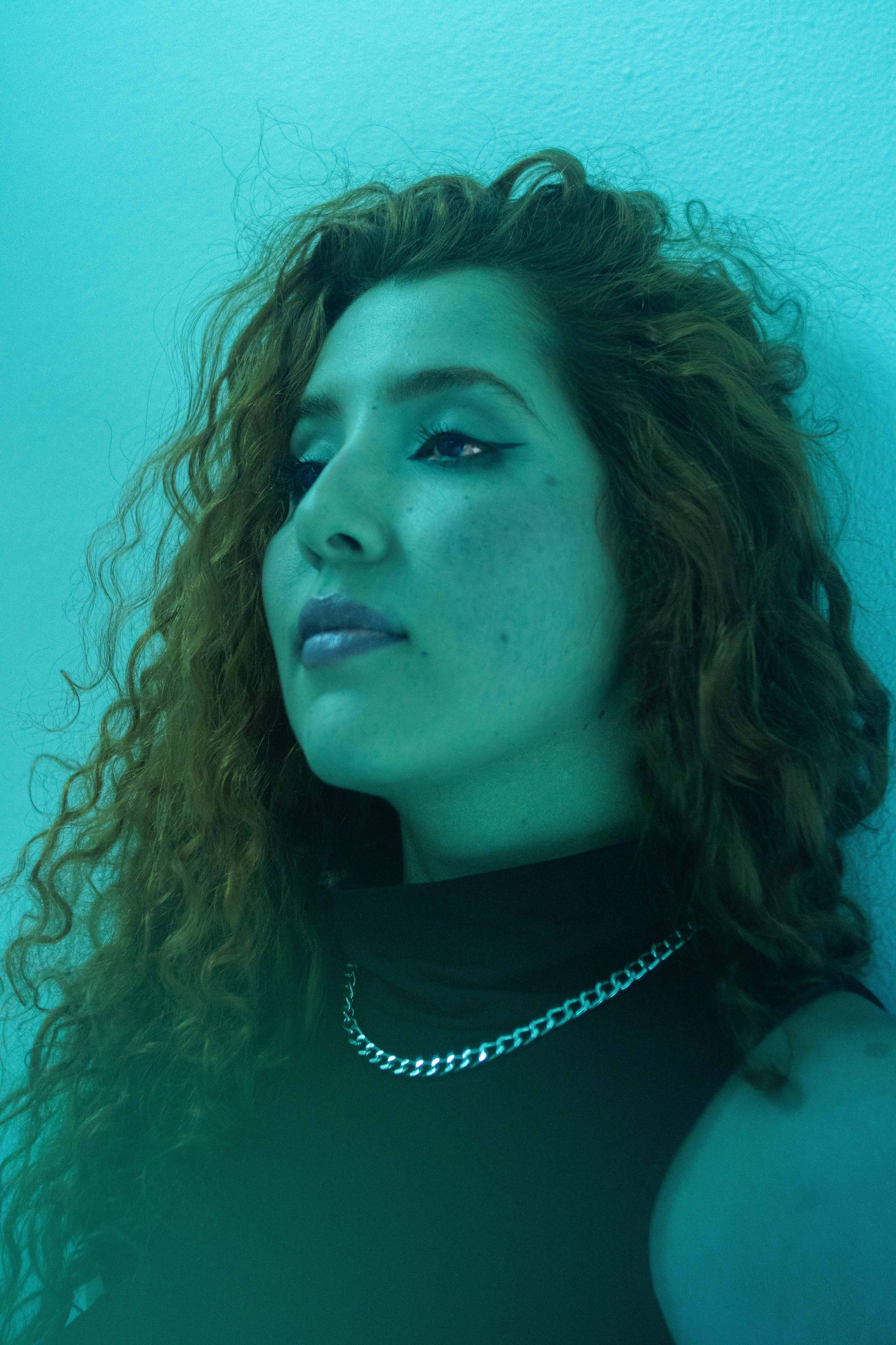 Stylish portrait of woman with curly hair in soft blue lighting