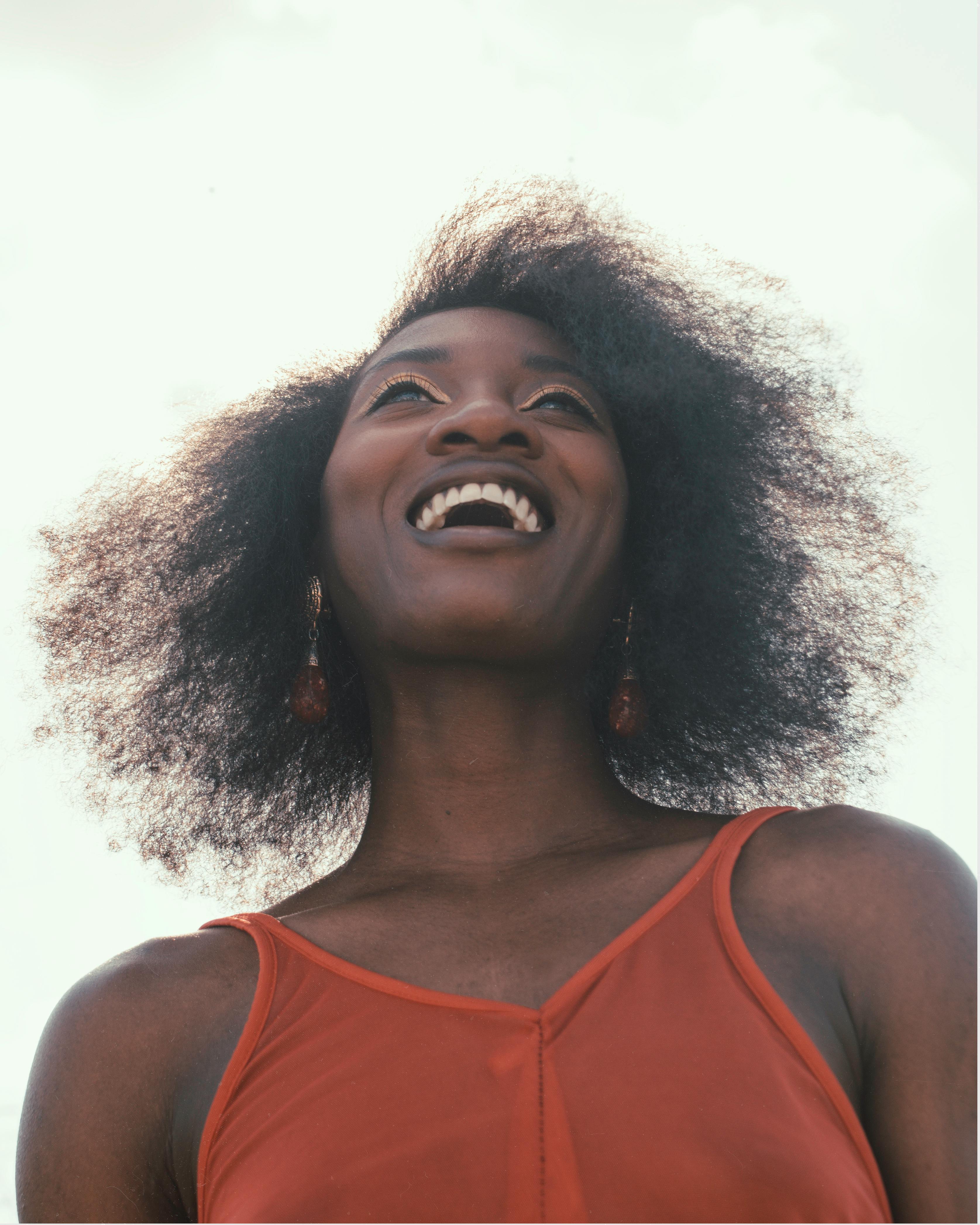 Smiling woman with afro hairstyle enjoying a bright day outdoors, radiating happiness.