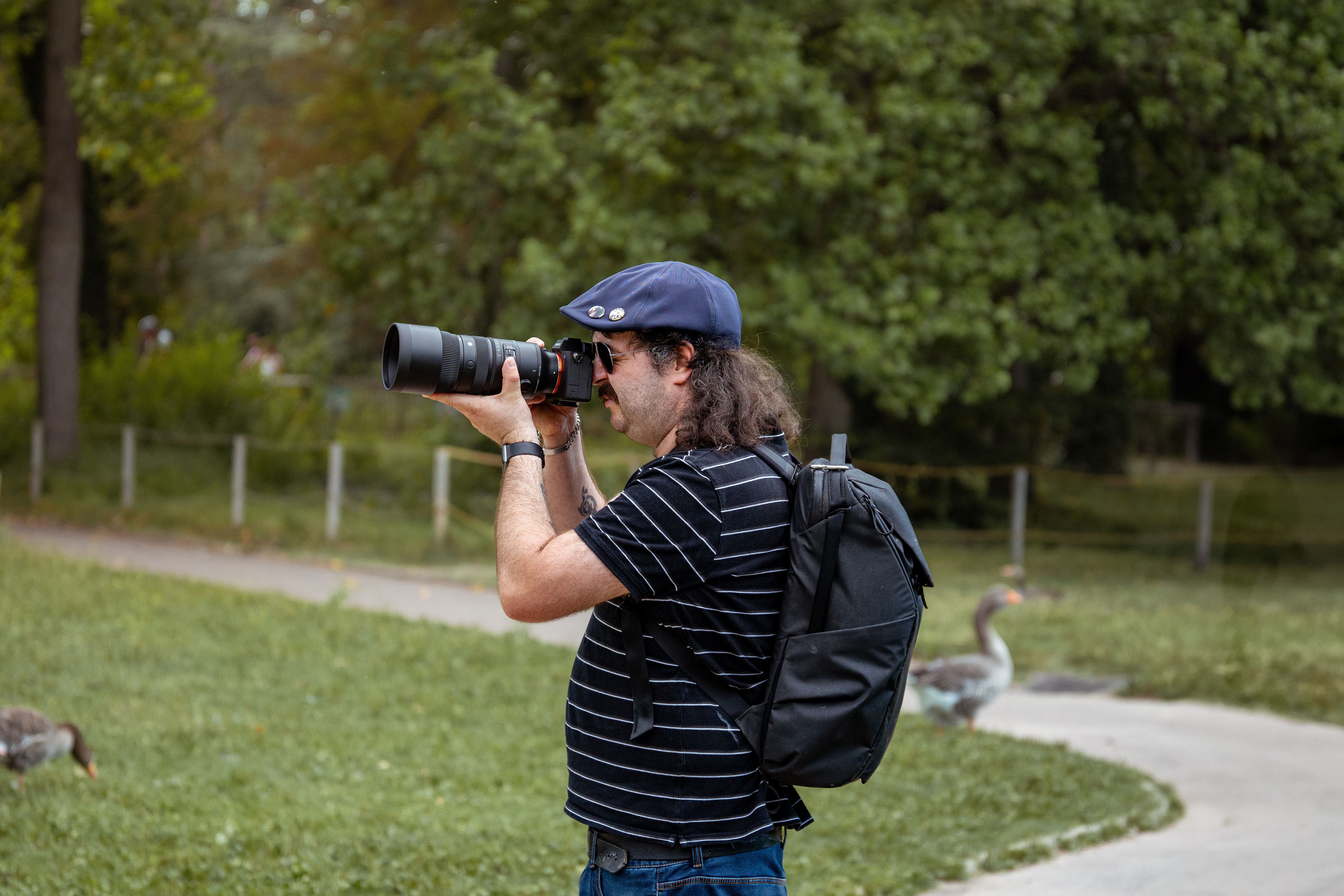 A photographer with a zoom lens takes pictures in a lush park setting, capturing nature's beauty.