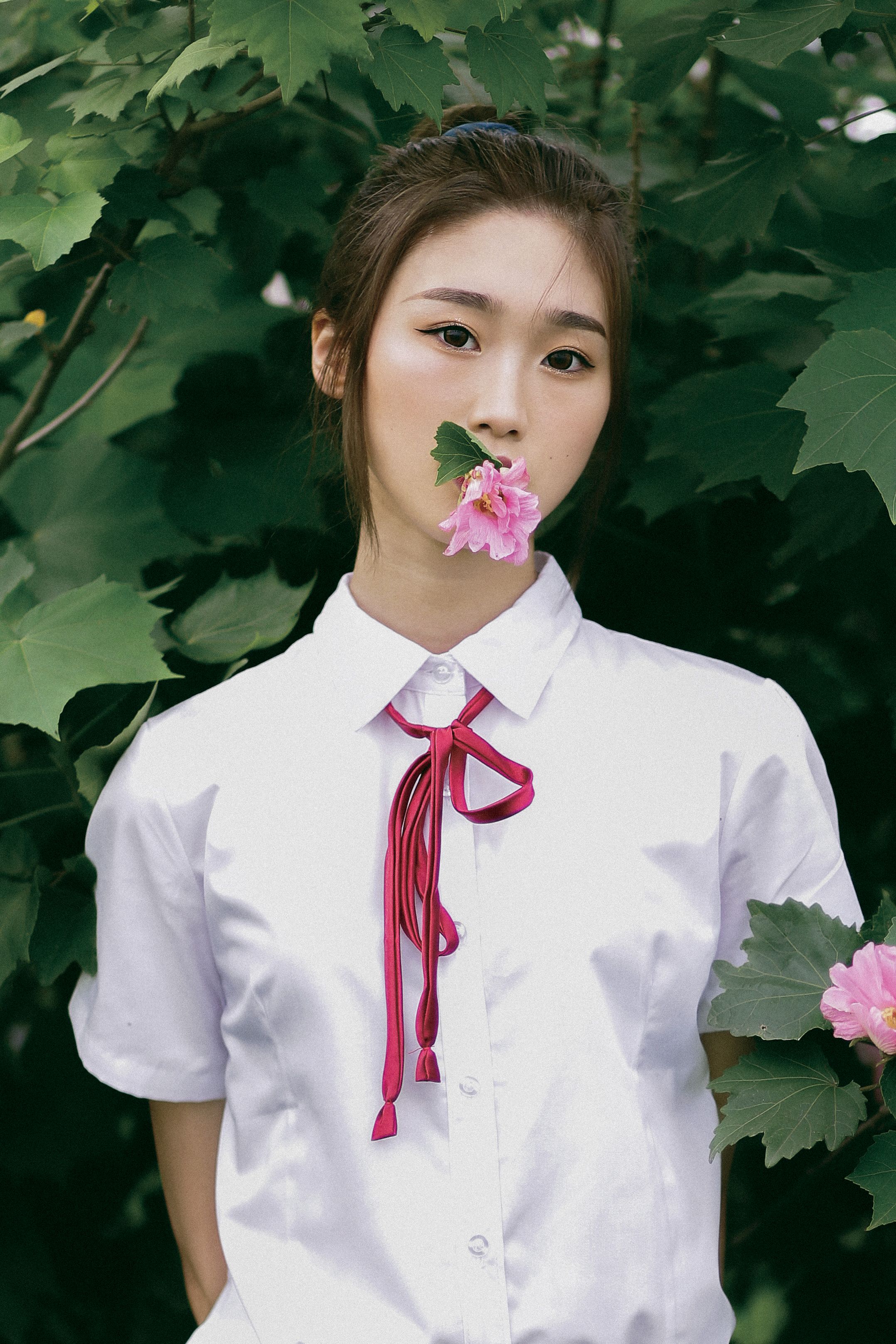 Portrait of a young woman in a white blouse holding a pink flower in nature.