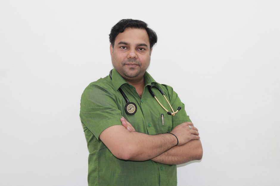 Portrait of a confident male doctor with stethoscope in a green shirt against a white background.