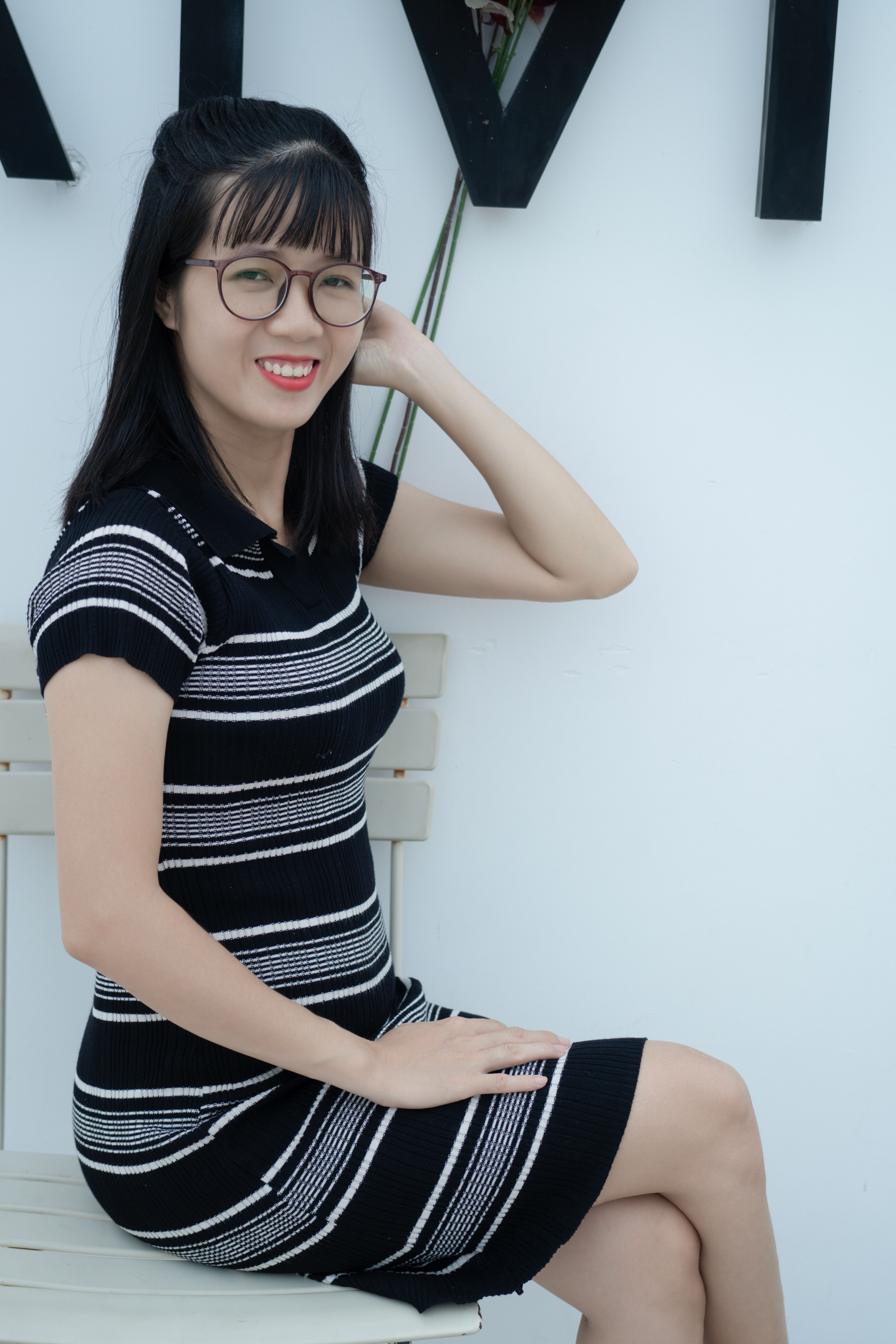 Smiling woman in glasses wearing a striped dress, seated indoors for a portrait photo.