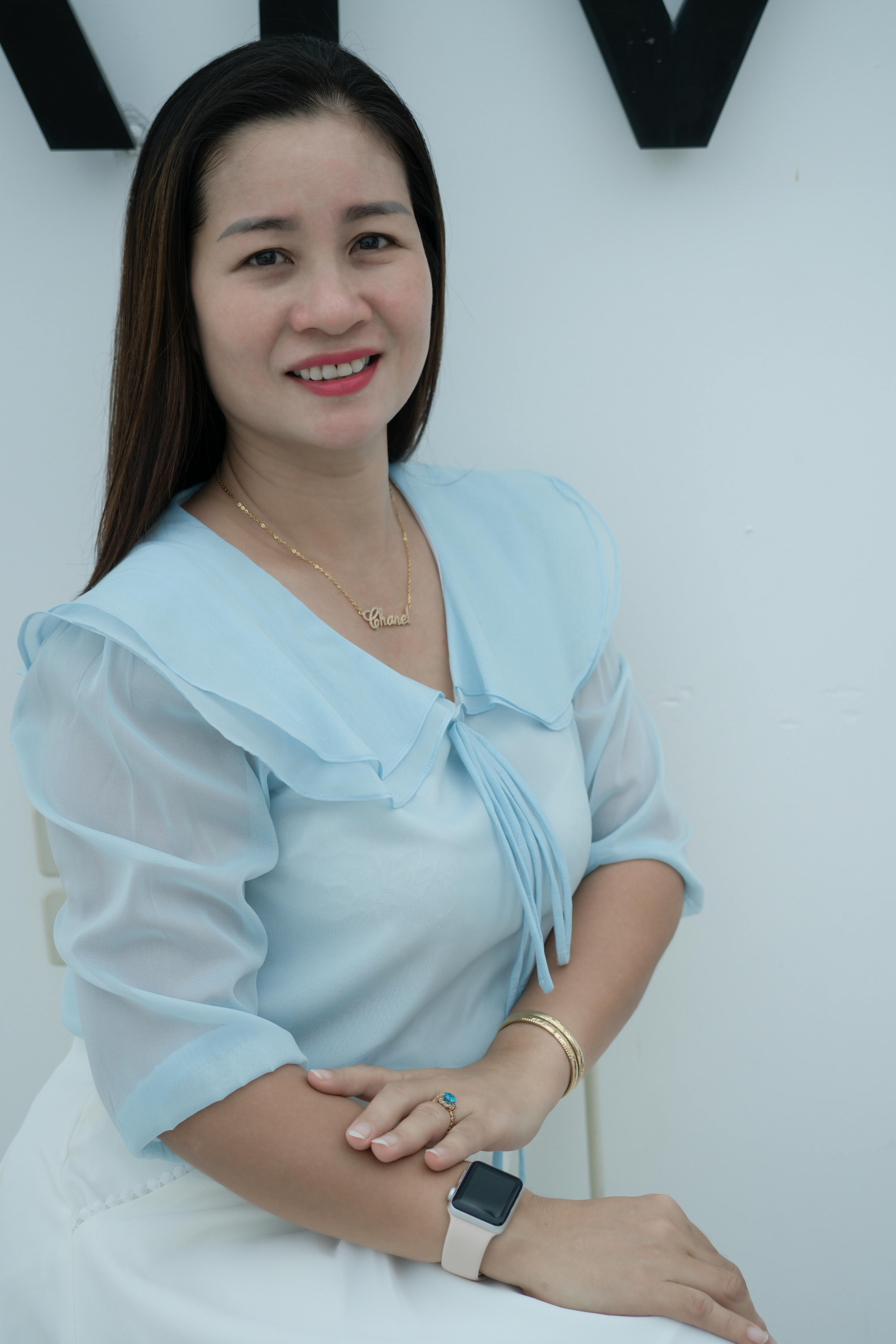 A relaxed portrait of a woman in a light blue blouse, smiling indoors.