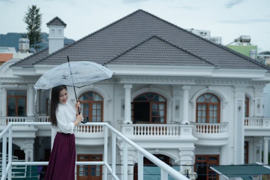 Elegant woman with umbrella standing in front of luxury mansion showcasing classic architectural design.