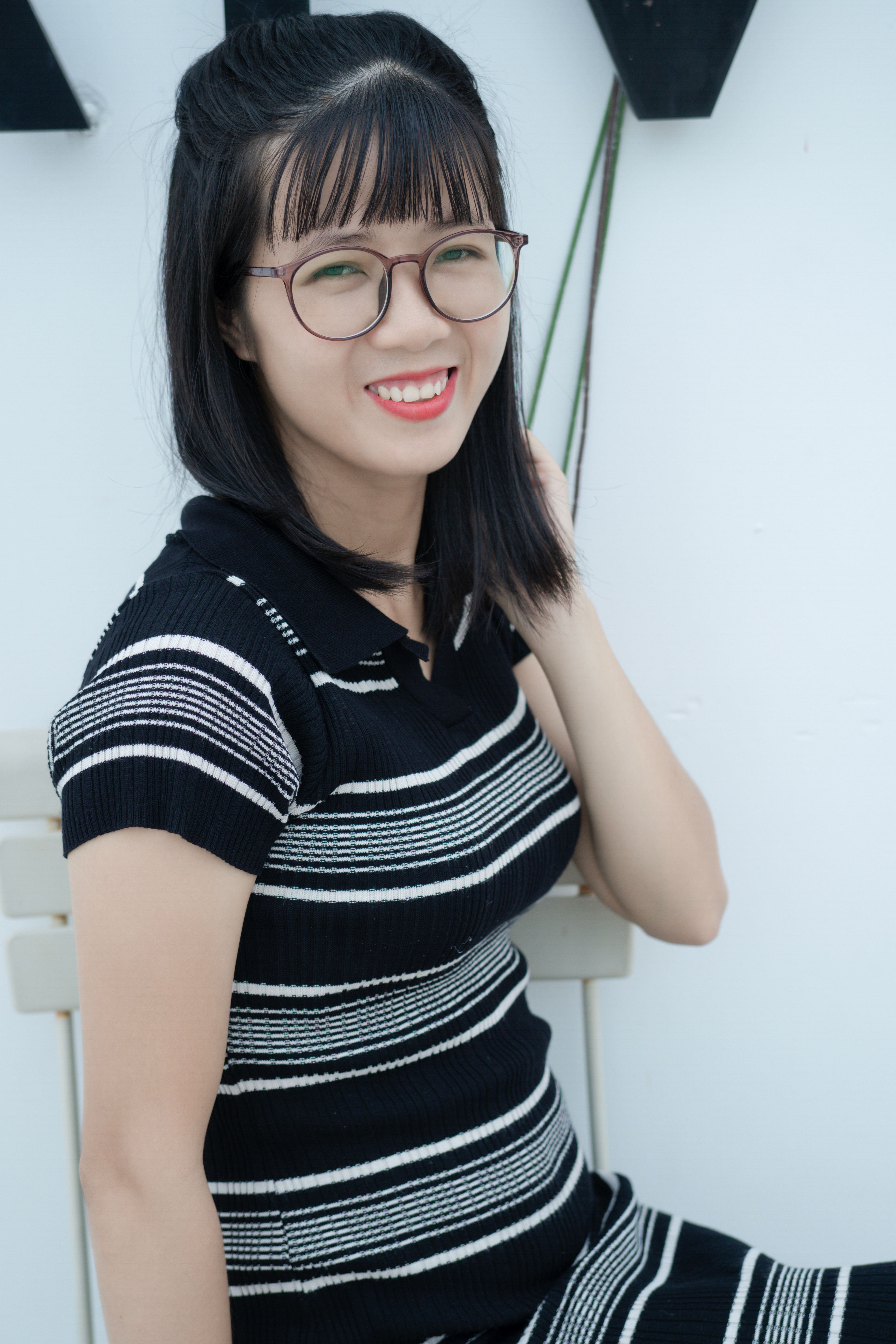 Happy young woman with glasses and striped black dress smiling indoors.