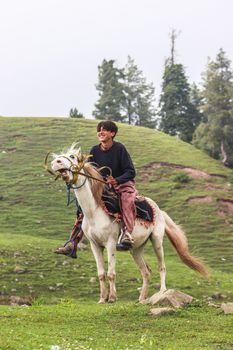 A joyful man riding a horse in the scenic green hills of Naran, Pakistan.