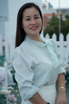 A woman in elegant attire smiling outdoors with a blurred garden background.