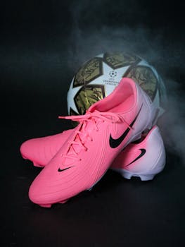 Photo of vibrant pink sports shoes with a soccer ball in the background and smoke effect.