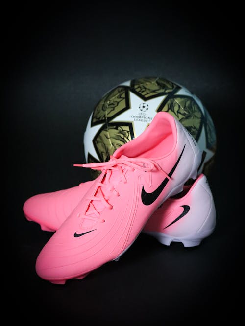 Free Bright pink soccer cleats paired with a Champions League ball on a dark backdrop. Stock Photo