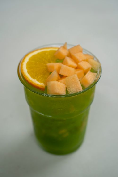 Free A vibrant glass of green juice topped with orange and melon, perfect for a refreshing summer drink. Stock Photo