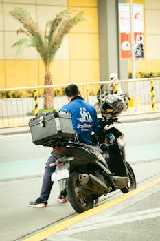 A delivery rider is seated on a motorcycle in an urban street setting, ready for the next delivery.