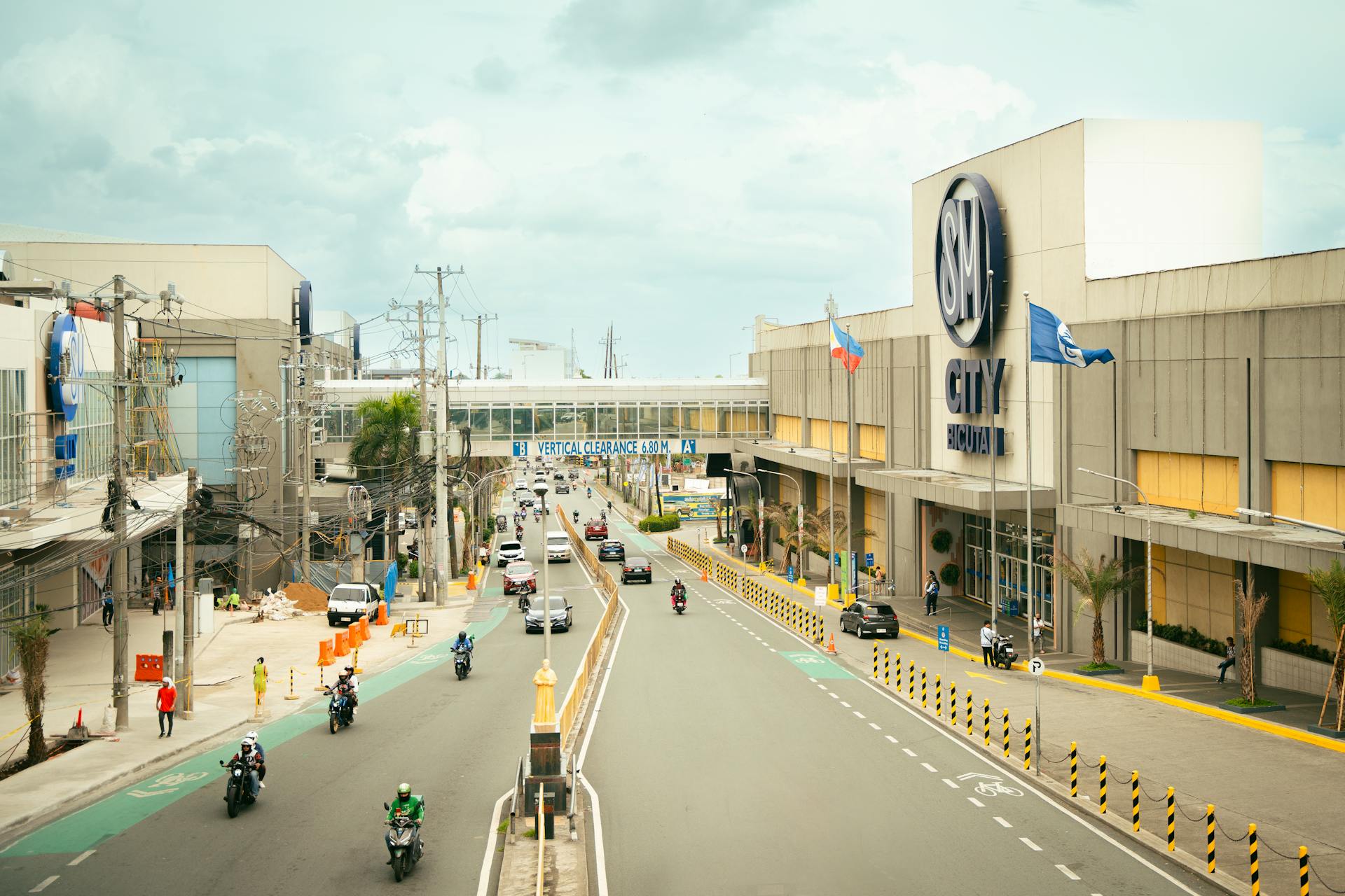 Traffic flows outside SM City Bacolod with motorcycles and cars under a cloudy sky.