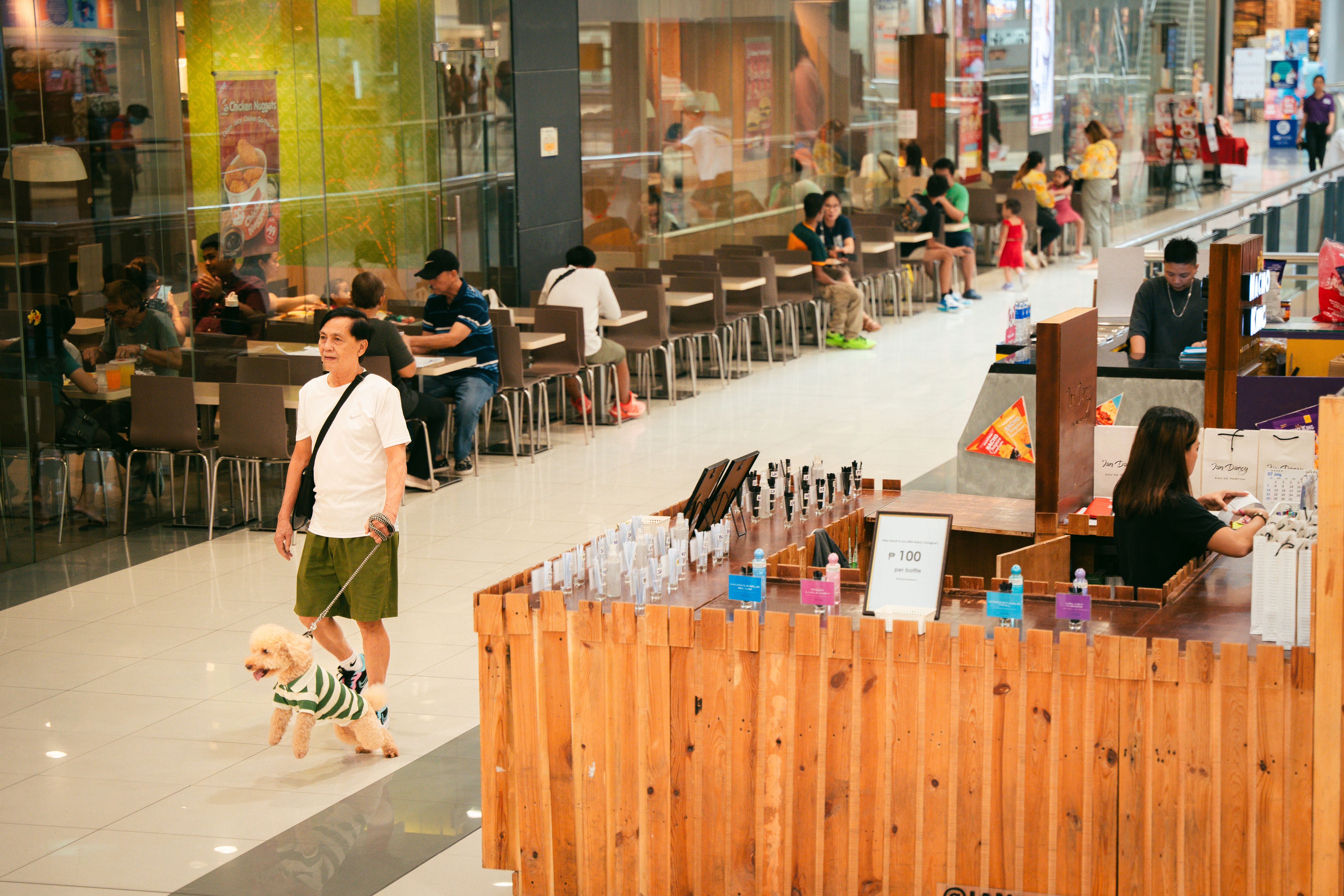 A lively indoor mall with people shopping and dining, featuring a man walking a dog.