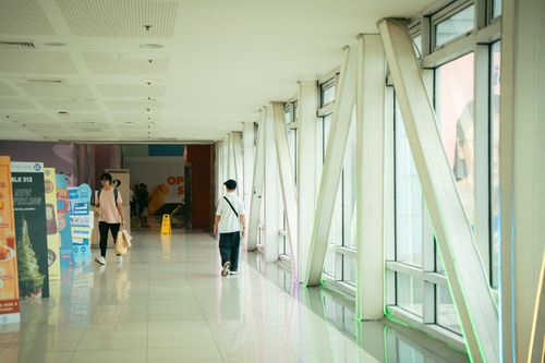 Free Indoor corridor with natural light, showing people walking and colorful posters. Modern architecture style. Stock Photo