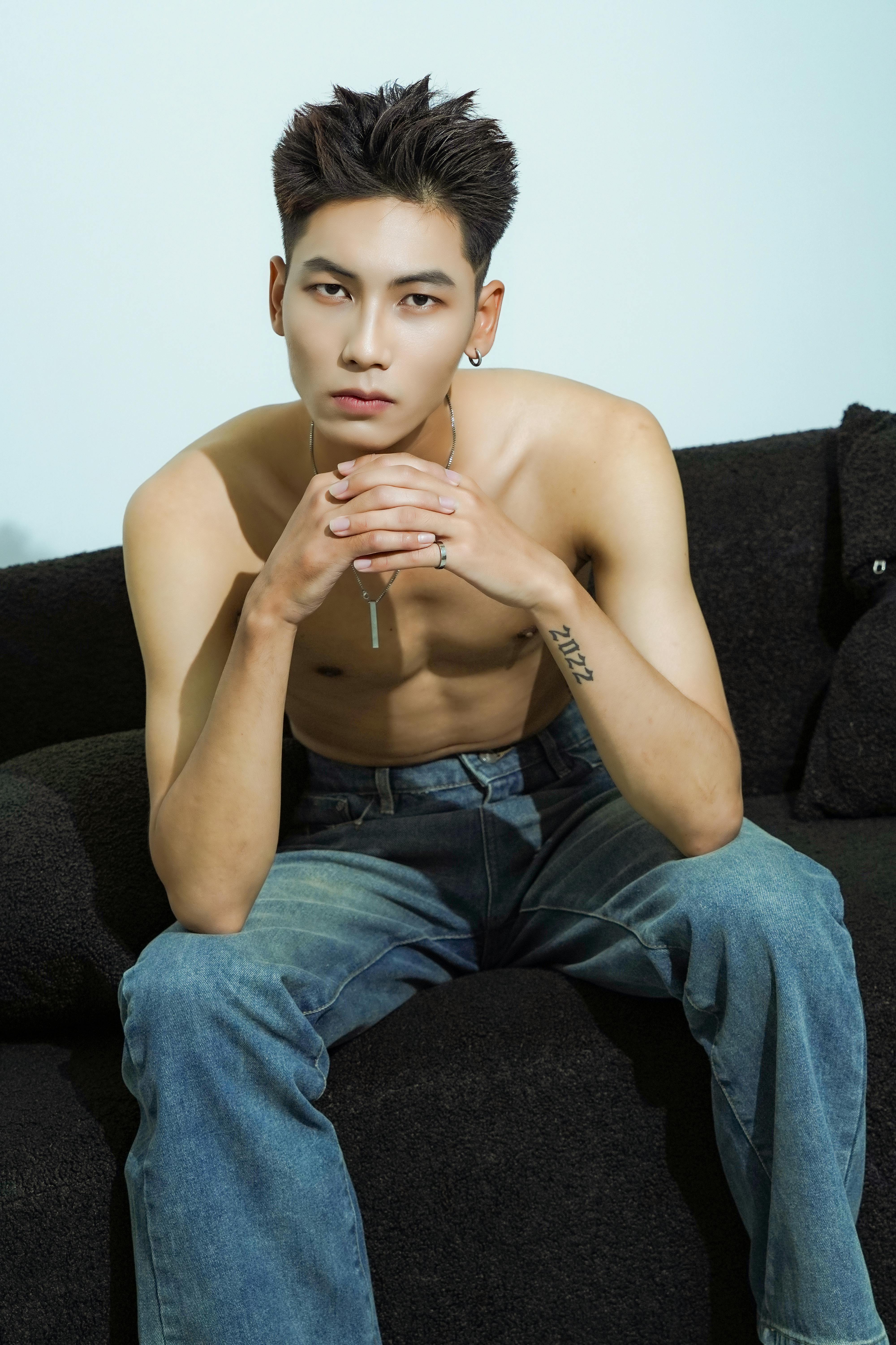 Young man seated on a black sofa with a serious look, exuding modern fashion style.
