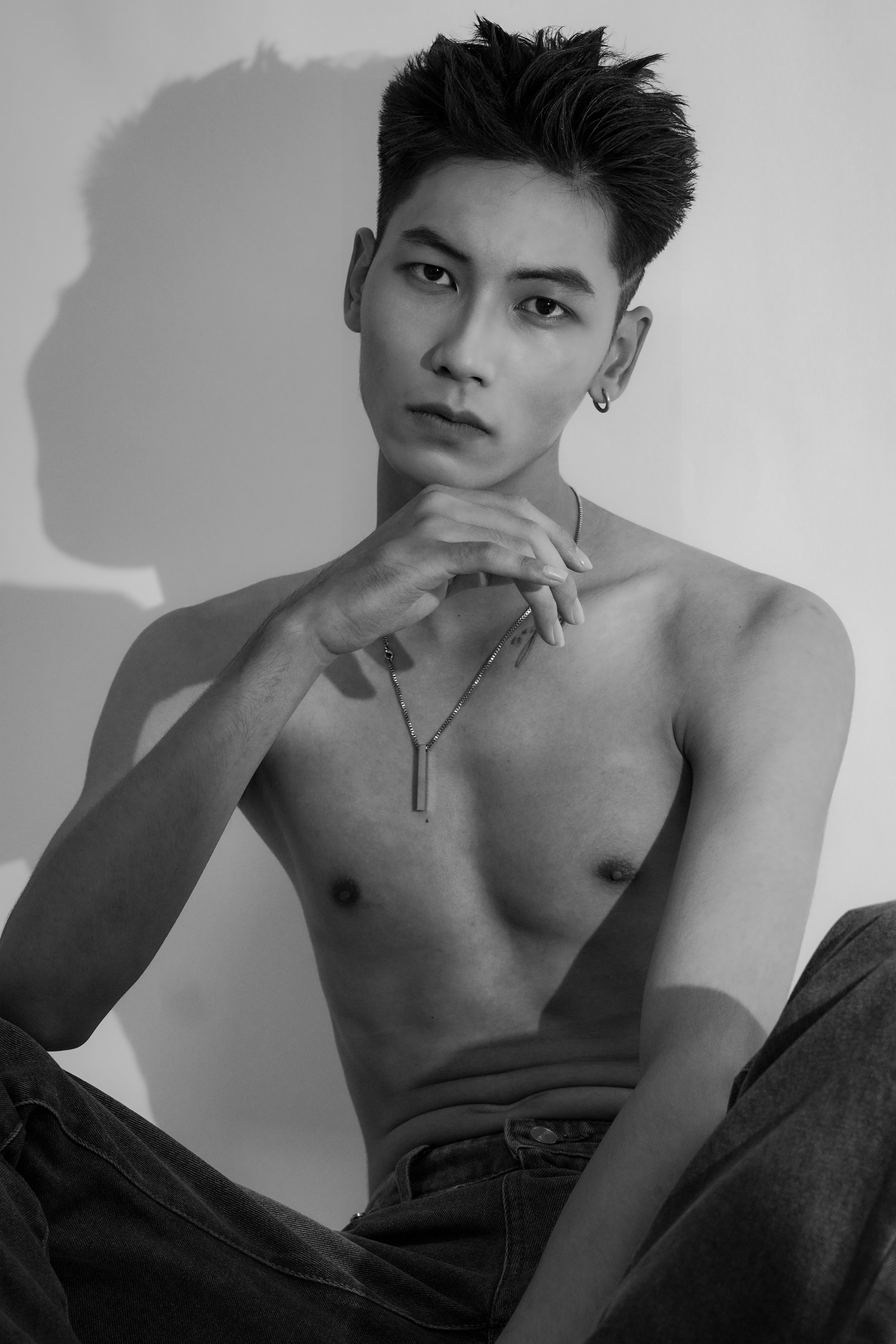 Monochromatic portrait of a shirtless Asian male model posing in a studio setting.