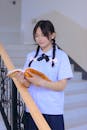 Student in Shirt Standing on Stairs and Reading Book