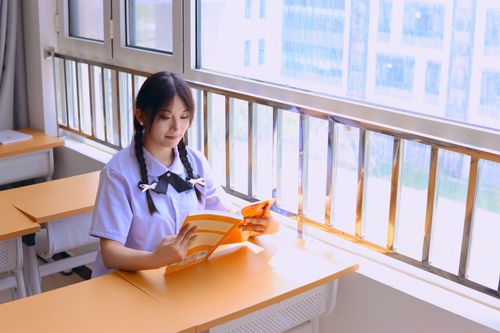 Free A young woman reads a book by the window in a bright, sunlit classroom. Stock Photo