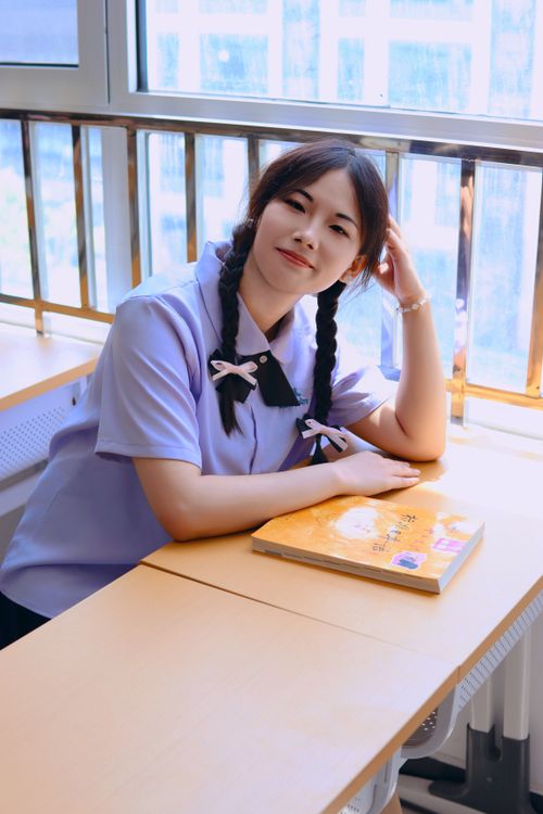 Free Smiling woman in school uniform sitting at a desk by a window in a bright room. Stock Photo