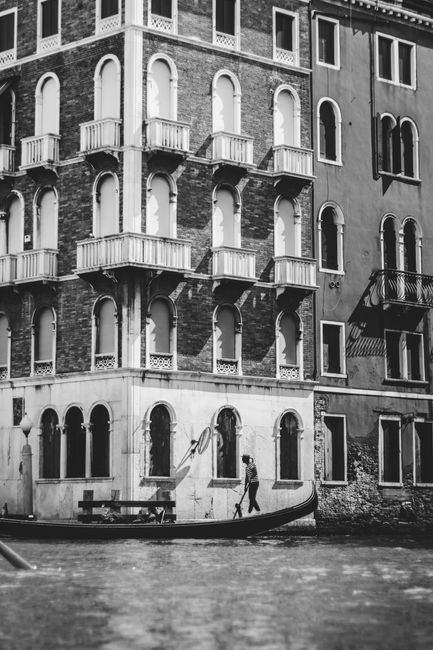 Black and white photo of a gondola on a canal in Venice, Italy, showcasing historic architecture.