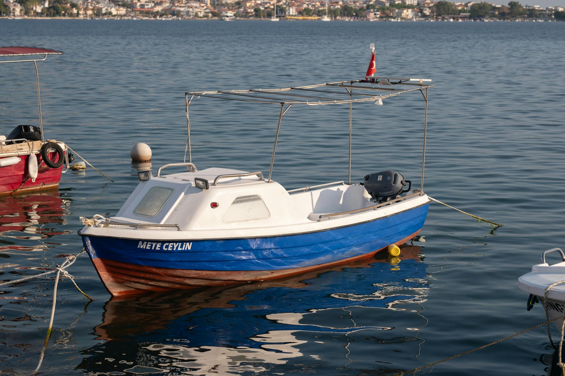 A small boat named 'Mete Ceylin' docked in a tranquil harbor in Foça, İzmir, Türkiye.