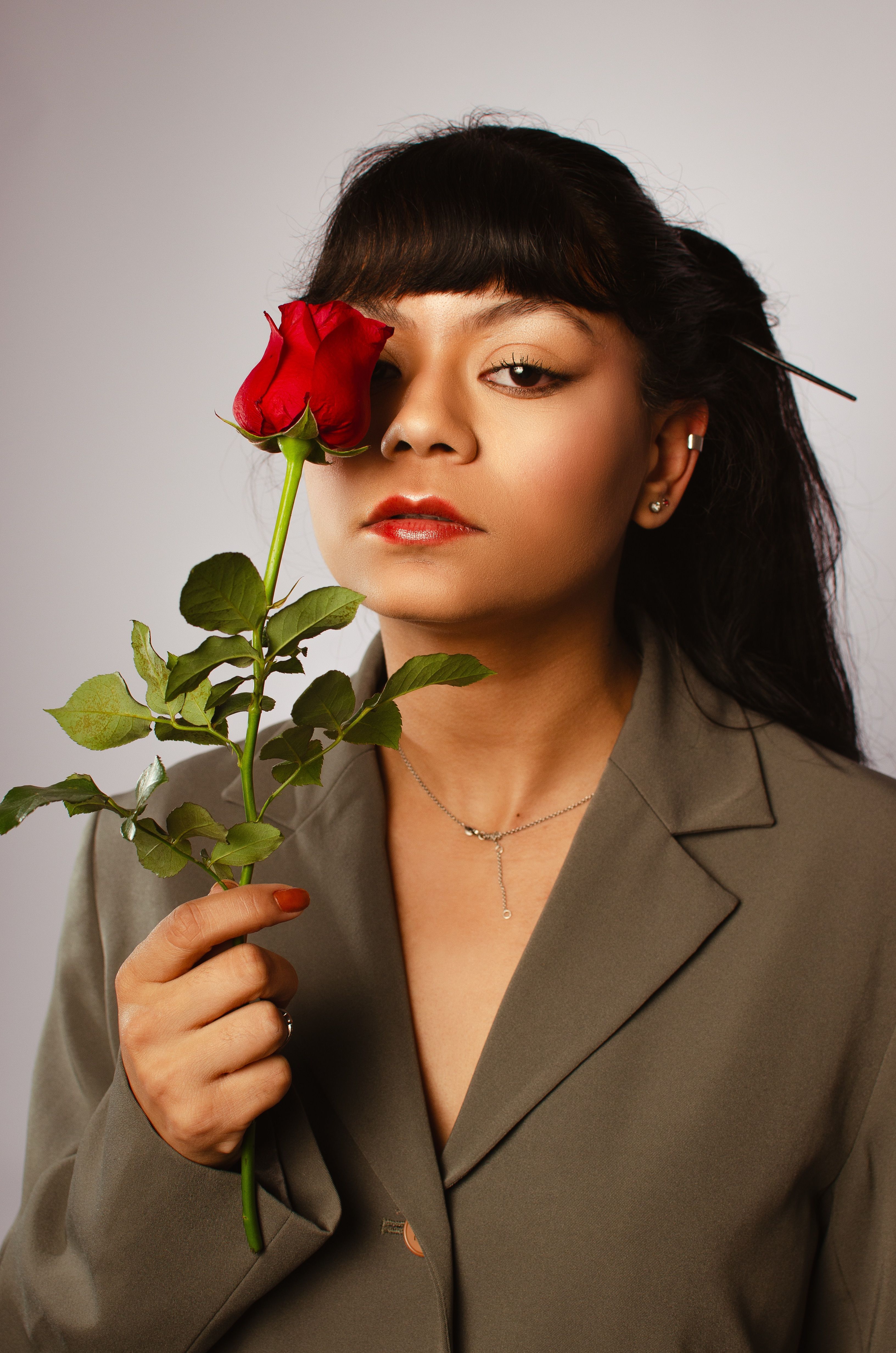 Sophisticated woman in studio with red rose, exuding elegance and glamour.