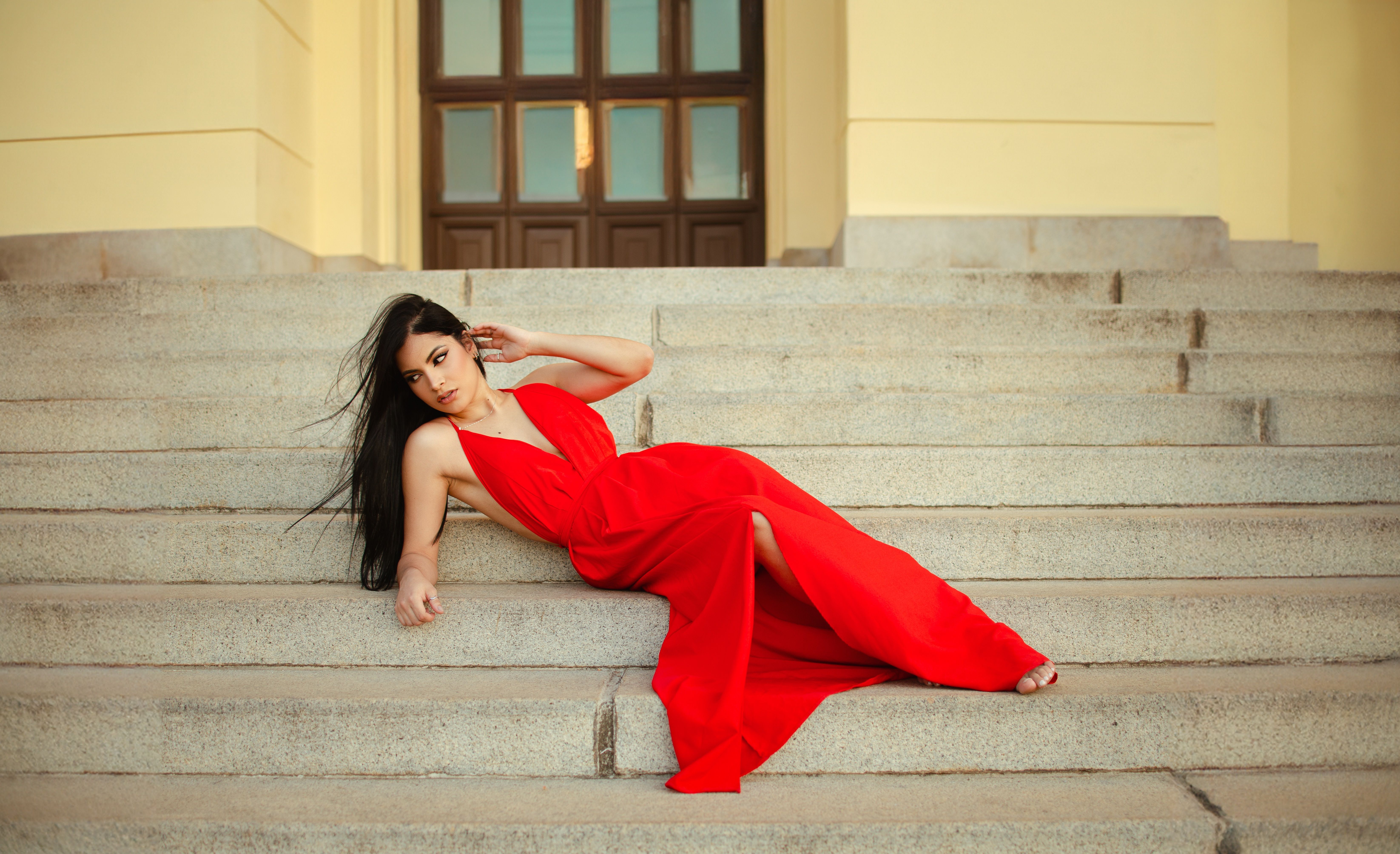 Stylish woman in a red gown lounging gracefully on steps indoors.