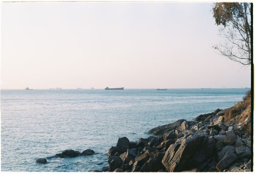 Free Peaceful ocean scene with cargo ships on the horizon, rocky shore foreground. Stock Photo