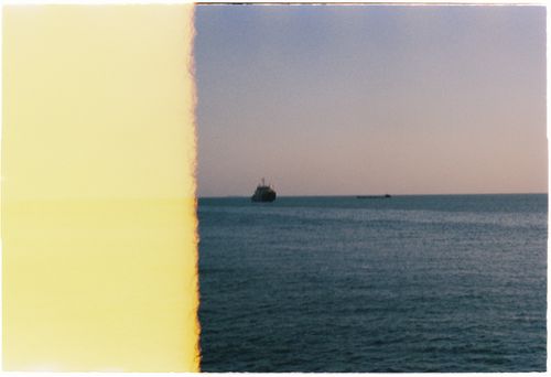 Free A vintage film photograph of a ship on the ocean at dusk with a unique light leak effect. Stock Photo