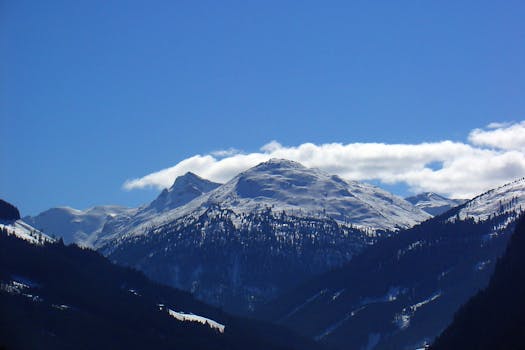 Majestic snow-covered mountain peaks under a clear blue sky with dramatic clouds.