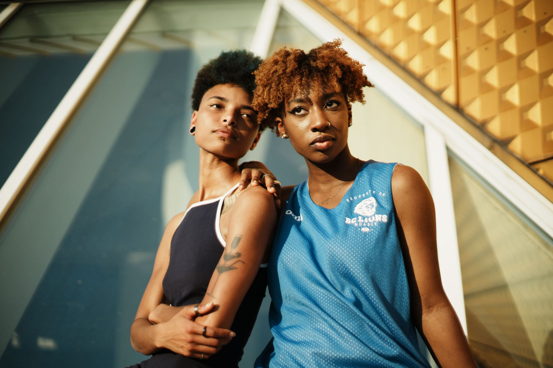Two black women with short curly hair in sportswear pose stylishly outdoors