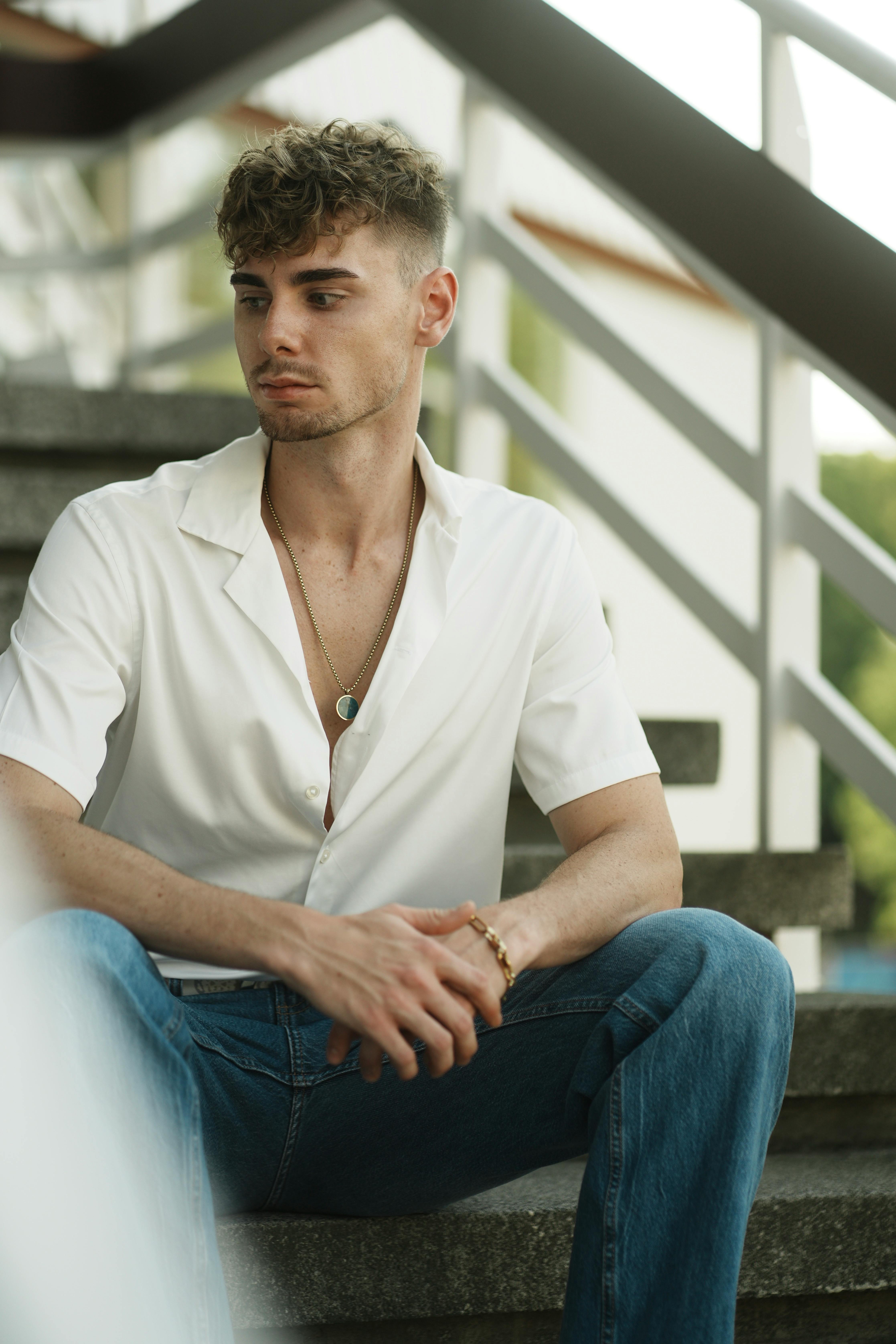 A young man in casual attire sitting pensively on steps outdoors.