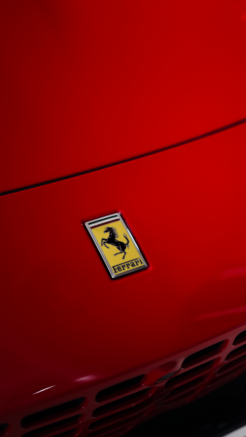 Free Detailed view of Ferrari logo on a glossy red car hood, showcasing luxury design. Stock Photo