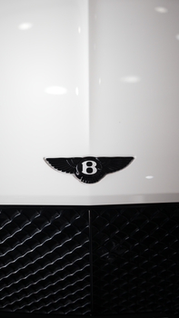 Close-up of a Bentley emblem on a sleek black grille. Modern, luxurious design.