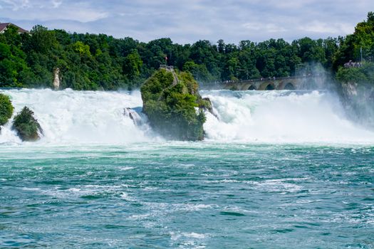 A breathtaking view of Rhine Falls surrounded by lush greenery under a clear summer sky.