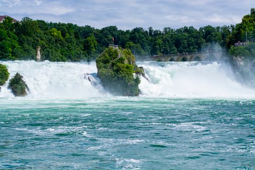 Free A breathtaking view of Rhine Falls surrounded by lush greenery under a clear summer sky. Stock Photo