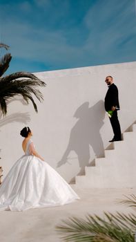 Bride and groom in stylish attire outdoors, capturing a romantic wedding moment on a white staircase.