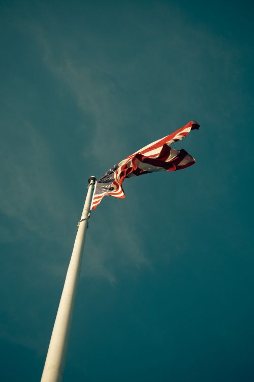 Free Low-angle view of an American flag waving on a flagpole against a clear blue sky, symbolizing patriotism. Stock Photo