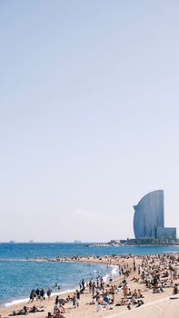 Crowded beach scene in Barcelona, Spain with clear skies and a view of the ocean.
